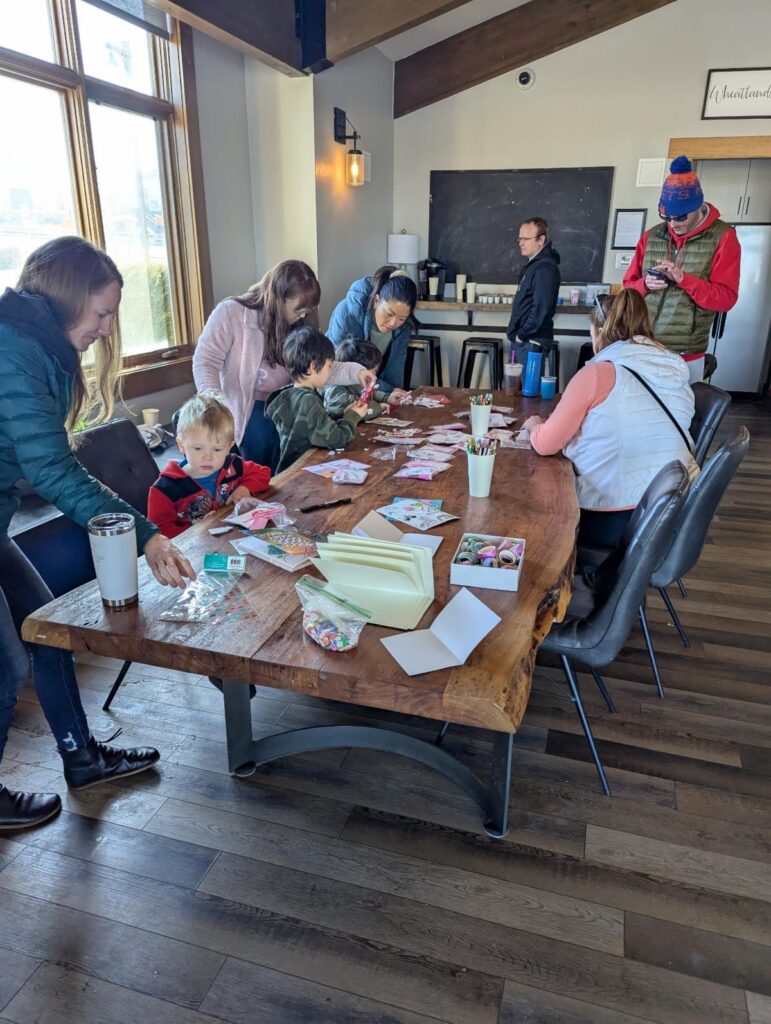 Group of people engaging in a crafting activity around a wooden table.