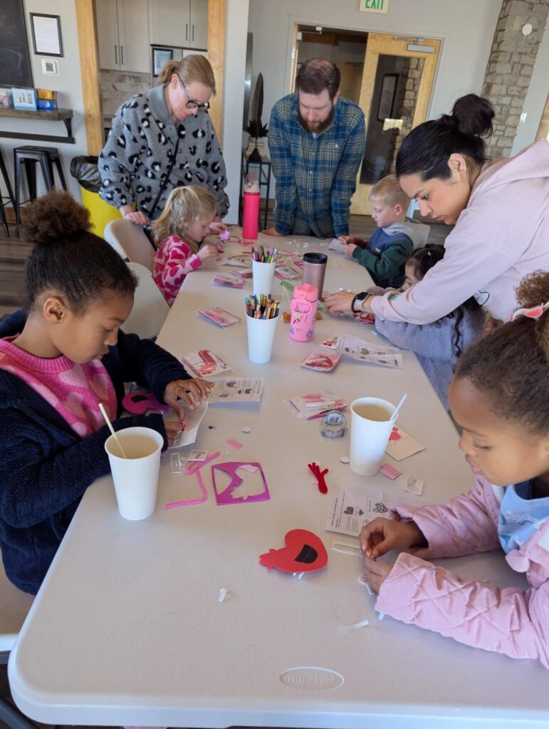 Children and adults at a table doing crafts in a cozy room.