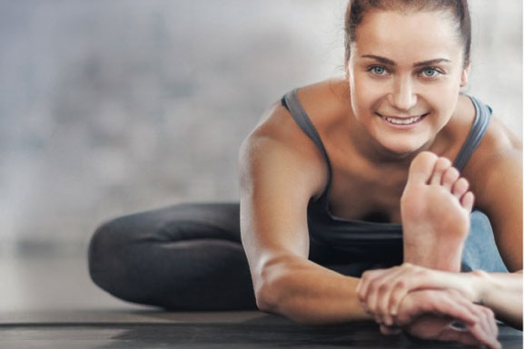 Women stretching with foot facing camera smiling.