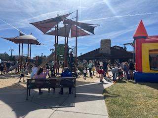 Outdoor playground with children and adults, a play structure with shade canopies, and an inflatable bounce house.