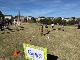 Children participating in a sack race on a grassy field with a "GAMES" sign in the foreground.
