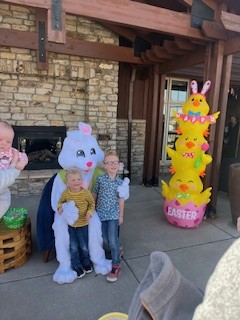 Two children with a person dressed as the Easter Bunny, next to an inflatable Easter decoration.